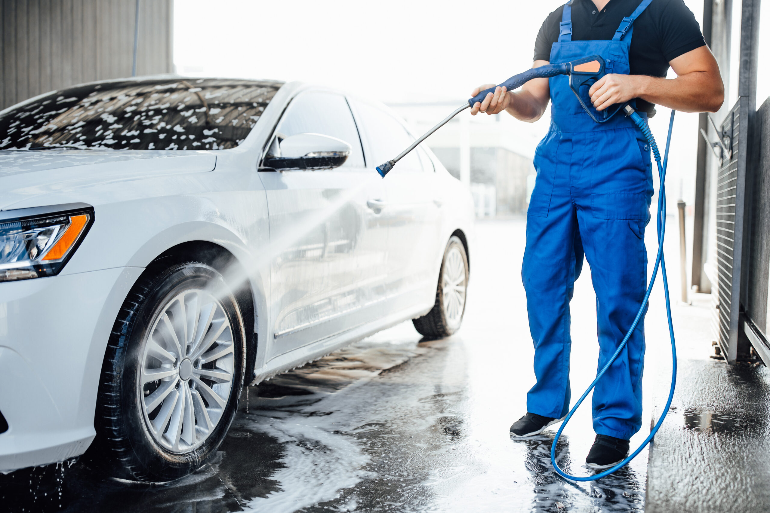 professional-washer-blue-uniform-washing-luxury-car-with-water-gun-open-air-car-wash